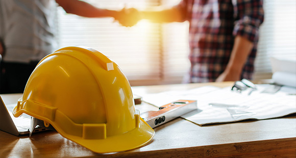 a yellow hardhat sitting on a table with two people shaking hands in the background